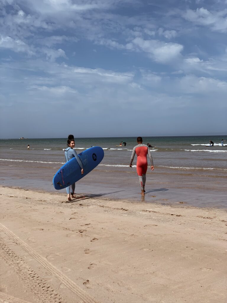 ragazza mora, con tavola da surf sotto il braccio, prima di una lezione sulla spiaggia di Essaouira